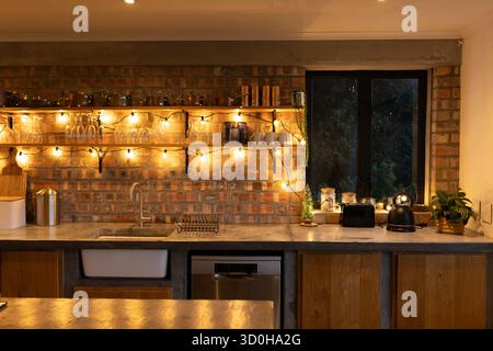 Die Betonarbeitsfläche verfügt über ein Waschbecken und einen Wasserhahn unter Holzregalen mit Lichterketten Stockfoto