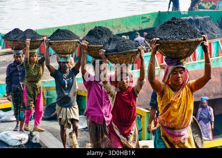 Dhaka, Bangladesch - 15. April 2024: Ein Blick auf Arbeiter, die schwere Mengen Kohle in gewebten Körben transportieren, eine düstere Szene, die die harte Realität der harten Arbeit vor dem Hintergrund industrieller Aktivitäten widerspiegelt. Stockfoto