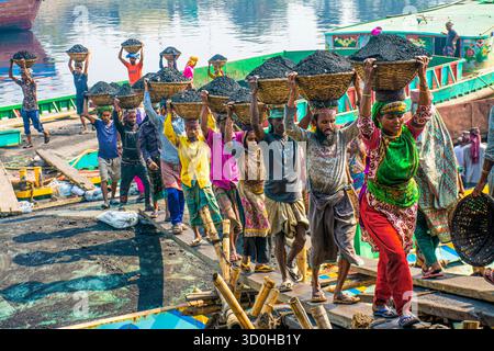 Dhaka, Bangladesch - 15. April 2024: Blick auf Arbeiter, die mit Kohle gefüllte Körbe auf ihren Köpfen tragen, eine Linie von leuchtenden Farben vor dem Hintergrund des Stockfoto