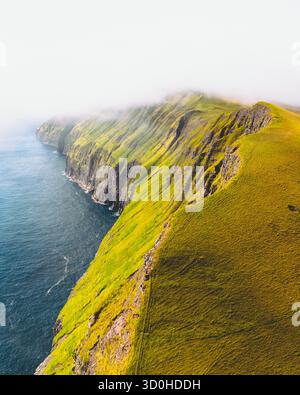 Aus der Vogelperspektive sehen Sie dramatische Klippen, die in smaragdgrünes Grün gehüllt sind, und tauchen Sie in das tiefblaue Meer ein, Trollkonufingur, Vagar und Färöer. Stockfoto