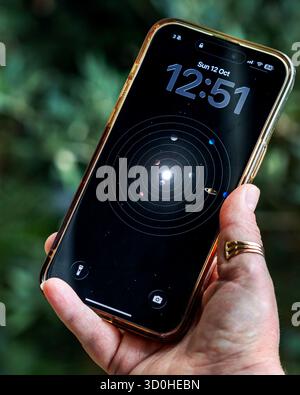 Das iPhone 15 Pro max wird von einer Kaukasierhand gehalten, zeigt den Sperrbildschirm der Planeten und die Zeit um 12:51 Stockfoto