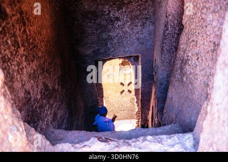 Ein Priester sitzt auf der Steintreppe zu einer Felsenhöhle in Lalibela, Nordenäthiopien. Stockfoto