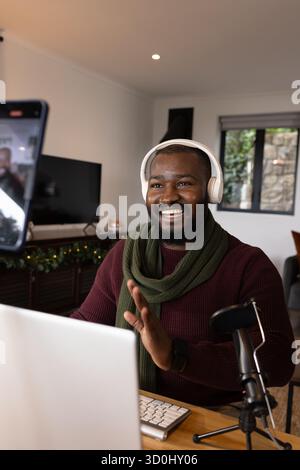 Afroamerikaner mittelgroßer Mann, der Kopfhörer mit Laptop, Mikrofon und Smartphone im Heimbüro trägt. Technologie, Arbeitsplatz, gemütlich, modern, kommunikativ Stockfoto