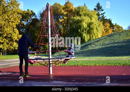 Vater spielt mit Kindern am sonnigen Herbstmorgen im Park auf einem roten Klettergerüst, Familie genießt gemeinsam Outdoor-Spaß. papa mit zwei Kindern Stockfoto
