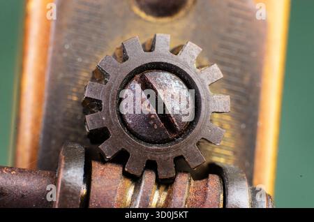 Extreme Makroansicht eines kleinen Metallstirnrads auf einem rostigen Schraubenkopf mit mechanischer Textur und industriellen Details. Stockfoto