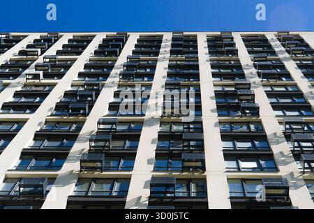 Abstrakter, flacher Blick auf eine moderne Hochhausfassade mit sich wiederholenden Fensterreihen und weißen Wänden unter klarem blauem Himmel Stockfoto