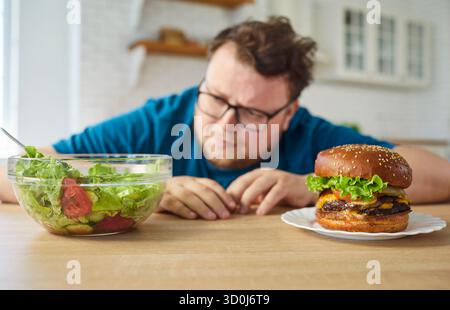 Die Wahl zwischen Burger und Gemüsesalat für übergewichtigen Mann mit Dilemma Stockfoto