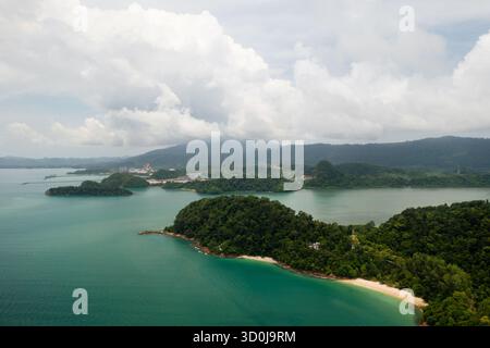 Türkisfarbenes Wasser hüllt sanft an ein sandiges Ufer, das von dichten grünen Hügeln umgeben ist. Diese ruhige Küstenszene fängt das Wesen eines tropischen Paras ein Stockfoto