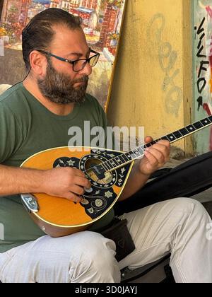 Ein einheimischer Straßenmusiker spielt traditionelle griechische Lieder auf einem Bouzouki-Gitarreninstrument auf dem Manastiraki-Platz in Athen, Griechenland Stockfoto