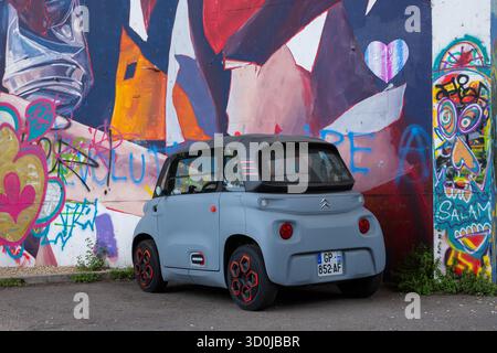 Poitiers, Frankreich - 2. August 2025: Ein kleines Citroen-Elektroauto parkt vor einer lebhaften Graffiti-Wand in Poitiers, mit farbenfroher Straßenkunst und Stockfoto