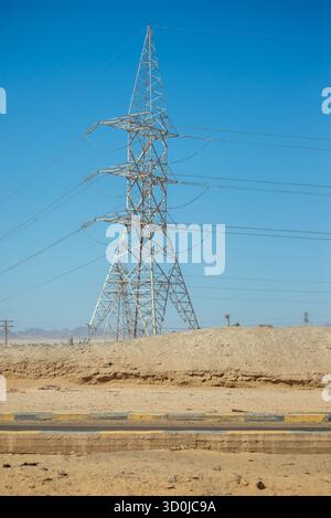 Ein hoher Stromübertragungsturm steht in der Wüstenlandschaft von Hurghada, Ägypten, mit Stromleitungen über dem klaren blauen Himmel Stockfoto