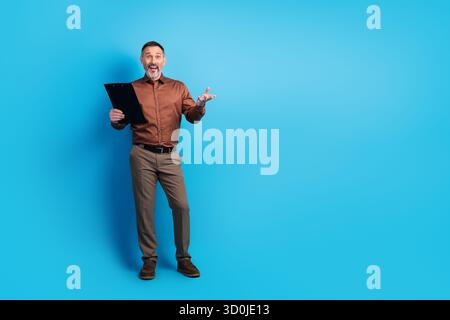 Reifer Geschäftsmann mit Klemmbrett spricht in einem hellblauen Studio mit Kamera und bietet ein professionelles Firmenporträt für Geschäftsbüros oder Unternehmen Stockfoto