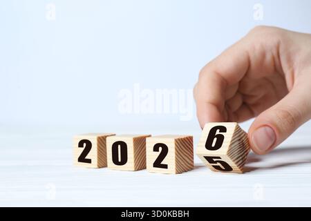 Neujahr. Frau, die den Würfel mit den Zahlen 5 und 6 umdreht, um 2026 auf weißem Hintergrund zu machen, Nahaufnahme Stockfoto