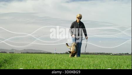 Eine Frau, die eine Sonnenbrille trägt, mit einem Schäferhund, einer Leine und grafischen Linien quer durch den Park Stockfoto