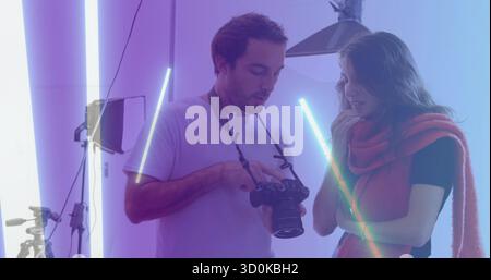 Hält DSLR-Kamera-Fotograf und Frau, die Bilder im Studio überprüft, mit rotem Schal und LED-Röhren Stockfoto