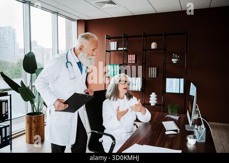 Heller klinischer Moment, als Oberarzt und Krankenschwester den Patienten konsultieren, während ein Kollege die Befunde am Computer in einem modernen Büro erklärt Stockfoto