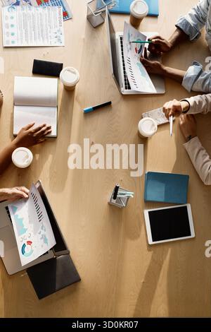 Manager, die ein Meeting im Büro haben. Direkt über dem Blick auf nicht erkennbare Personen, die mit Laptop, Papieren und Kaffee an einem großen Tisch sitzen Stockfoto