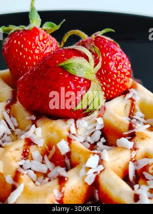 Nahaufnahme einer Waffel mit Kokosflocken, Erdbeeren und Schokoladensirup. Stockfoto