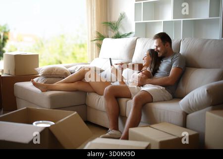 Glückliches Paar, das sich ausruht, während er nach Hause zieht und auf einer Couch sitzt Stockfoto