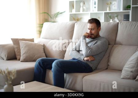 Trauriger Mann, der allein auf einer Couch zu Hause sitzt Stockfoto