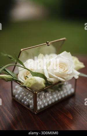 Weiße Rosenknospen in einer Glasbox für Eheringe Stockfoto