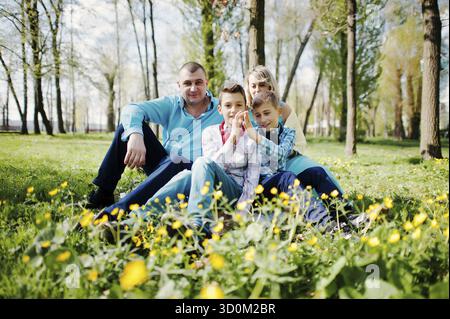 Glücklich schwanger Familie mit zwei Söhnen, gekleidet in eine türkise Kleidung, sitzen auf dem Rasen mit Blumen im park Stockfoto