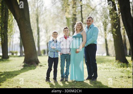 Porträt von glücklich schwanger Familie mit zwei Söhnen, gekleidet in einen türkisfarbenen Kleidern im park Stockfoto