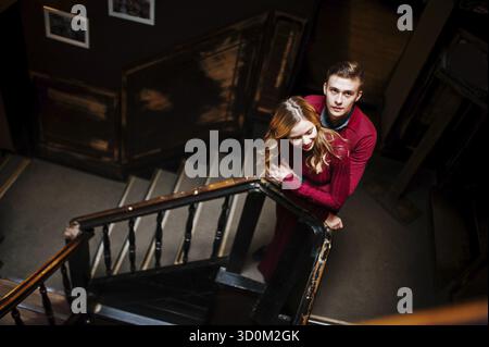 Schöne stilvolle Pärchen in einem roten Kleid in große Vintage Holztreppen Stockfoto