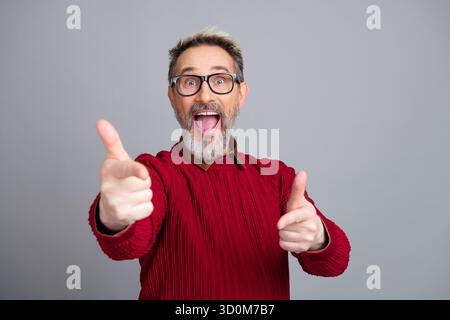 Fröhlicher Mann mittleren Alters in einem roten Pullover, der enthusiastisch mit ausdrucksstarker Aufregung gestickt Stockfoto