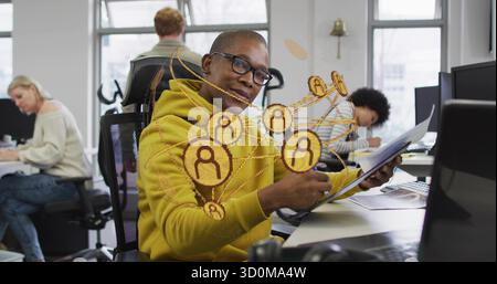 Schwarzer Mann mit gelbem Hoodie, der ein Tablet hält, das Dokumente im Büro mit Netzwerksymbolen anzeigt Stockfoto