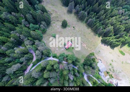 Aus der Vogelperspektive eines einsamen Hauses mit rotem Dach, eingebettet in eine Lichtung, umgeben von einem dichten Wald aus grünen Bäumen, geteilt von gewundenen Straßen, La Chaux-de-Fonds, Schweiz. Stockfoto