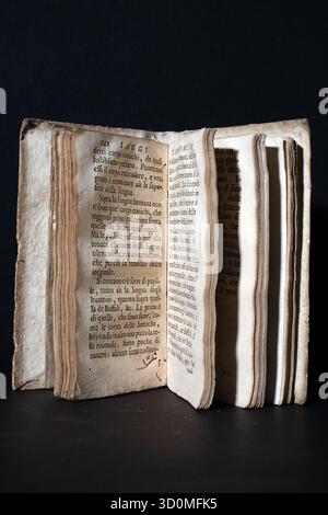Offene Seiten eines sehr alten, abgenutzten Buches (Frühdruck), auf dem veraltetes, gelbliches Papier mit ausgefransten Kanten zu sehen ist. Zeigt sichtbaren Text in altem Italienisch/Latein an. Stockfoto