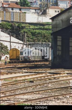 P, Portugal, Lissabon, 20. 03. 1993: Ein Zug der Vorortbahn der staatlichen Eisenbahngesellschaft CP Urbanos de Lisboa, der hauptsächlich von Pendlern genutzt wird, unterquert einen Stadtteil in einem Tunnel. Auf der rechten Seite ein Depot der Lissabonner Vorortbahn. [Automatisierte Übersetzung] Stockfoto