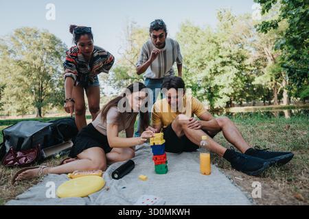 Gruppe von Freunden, die während eines sonnigen Picknicks im Park einen farbenfrohen Blockturm bauen Stockfoto