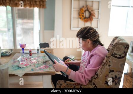 Junge Frau, die bunte Kunstwerke kreiert, während sie an ihrem Heimtisch sitzt Stockfoto