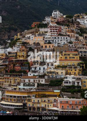 Aus der Vogelperspektive fallen bunte Häuser auf den grünen Hügel, eine Symphonie aus Ocker, weiß und Terrakotta gegen das tiefgrüne Laub, Positano, Kampanien, Italien. Stockfoto