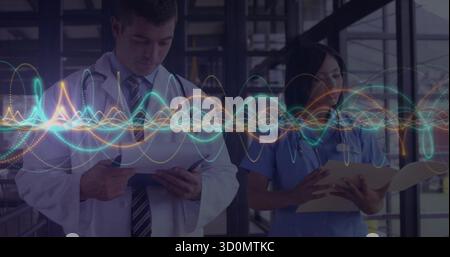 Mithilfe von Tablet und Datei konsultieren Mitarbeiter mit Stethoskopen im Stationskorridor und zeigen die Signalform an Stockfoto