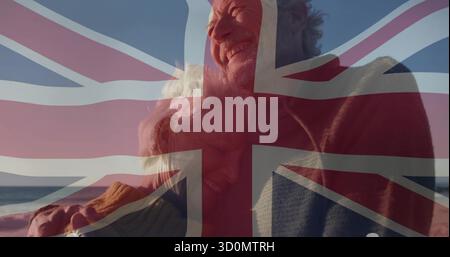 Älteres Paar umarmt Pullover am Strand mit Blick auf das Meer, mit halbtransparentem Union Jack Überzug Stockfoto