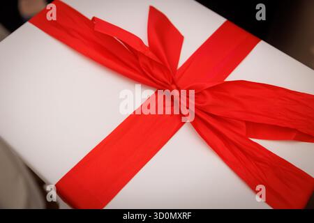 Nahaufnahme des Geschenkes mit breitem rotem Satinband, das in einer Schleife auf weißem Hintergrund gebunden ist. Stockfoto