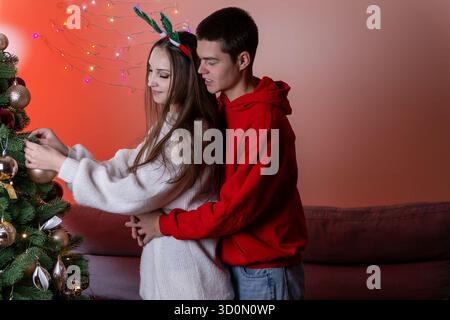 Junger Mann und Frau, die einen Weihnachtsbaum mit bunten Ornamenten dekorieren Stockfoto