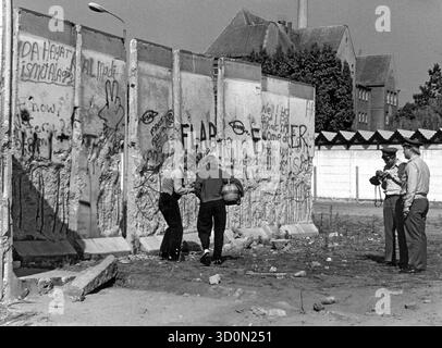 DEU, Deutschland, Berlin, 18.03.1990: Mauerspechte manipulieren die bereits bröckelnde Mauer an der Kiefholzstraße zwischen den Stadtteilen Neukoelln und Treptow. Zwei Mitglieder der DDR-Grenztruppen versuchen, das Geschehen filmisch festzuhalten. [Automatisierte Übersetzung] Stockfoto