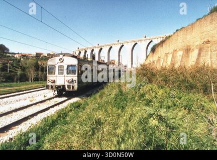 P, Portugal, Lissabon, 20.03.1993: Älterer Triebwagen von Alstom für die Lissabonner Vorortbahn, die von der staatlichen Eisenbahngesellschaft CP Urbanos de Lisboa betrieben wird und hauptsächlich von Pendlern genutzt wird. Das Bild zeigt den Zug, der unter einem Aquadukt in der Stadt fährt. [Automatisierte Übersetzung] Stockfoto