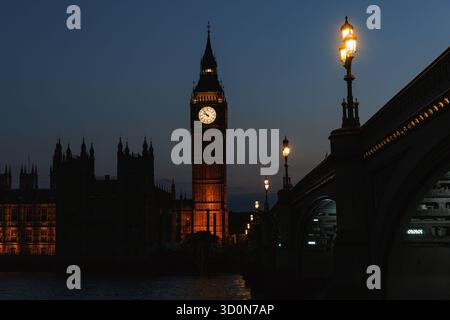 Nächtlicher Blick auf Big Ben und Westminster Bridge mit leuchtenden Straßenlaternen und Reflexionen auf der Themse. Stockfoto