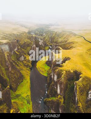 Aus der Vogelperspektive eines sich windenden Flusses, der durch einen tiefen Canyon mit moosbedeckten Klippen unter einem trüben Himmel schneidet, Fjaorargljufur, Island. Stockfoto