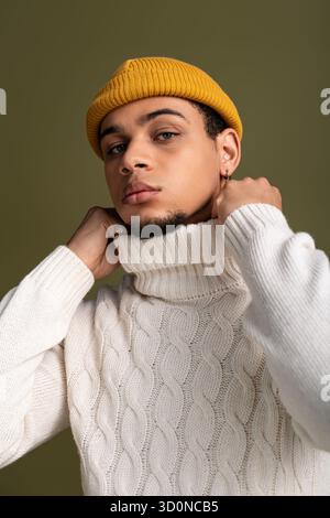 Ein hübscher junger Mann posiert selbstbewusst in einem gemütlichen Rollkragenpullover und einer hellen Mütze. Stockfoto