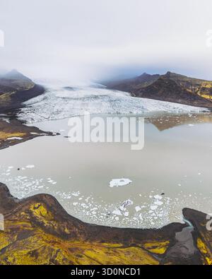 Aus der Vogelperspektive trifft auf das trübe Wasser der Lagune, ein starker Kontrast zur zerklüfteten, goldbraunen Landschaft, Svínafellsjökull Sveitarfélagið Hornafjörður, Island. Stockfoto