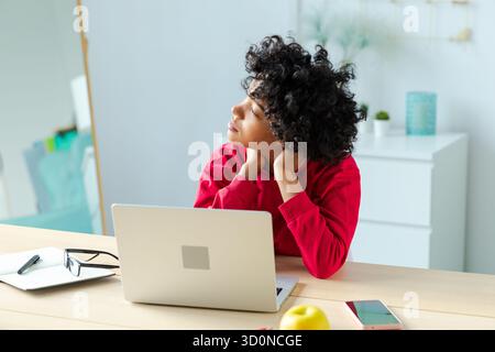 Verschlafene traurige Afroamerikanerin, die mit Laptop am Tisch sitzt. Müde überarbeitetes Mädchen faul zur Arbeit. Geschäftsstudentin, die sich nach der Arbeit am Laptop im Home Office langweilig erholt hat Stockfoto