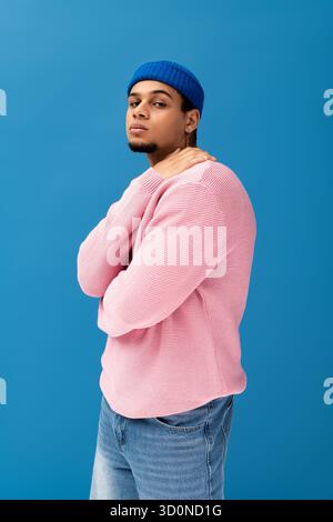 Ein hübscher junger Mann, der einen pinken Pullover und eine blaue Mütze trägt, posiert selbstbewusst. Stockfoto