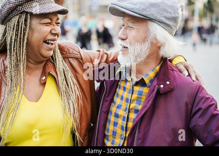 Multirassisches Seniorenpaar, das Spaß im Freien mit Stadt im Hintergrund hat - Liebe, Beziehung und fröhliches Lebensstil älterer Menschen Stockfoto