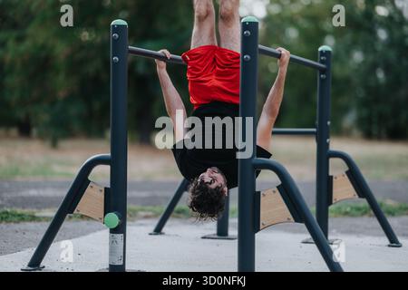 Mann auf dem Kopf in der Fitnessbar im Freien, der im Park Hängeübungen macht Stockfoto
